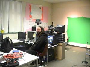 A person sitting at a desk with a green screen behind him

Description automatically generated